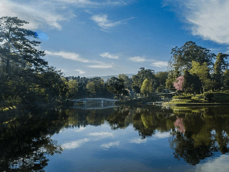 Ward's Lake Shillong — arched footbridge over calm waters with manicured gardens and misty Meghalaya hills in the background